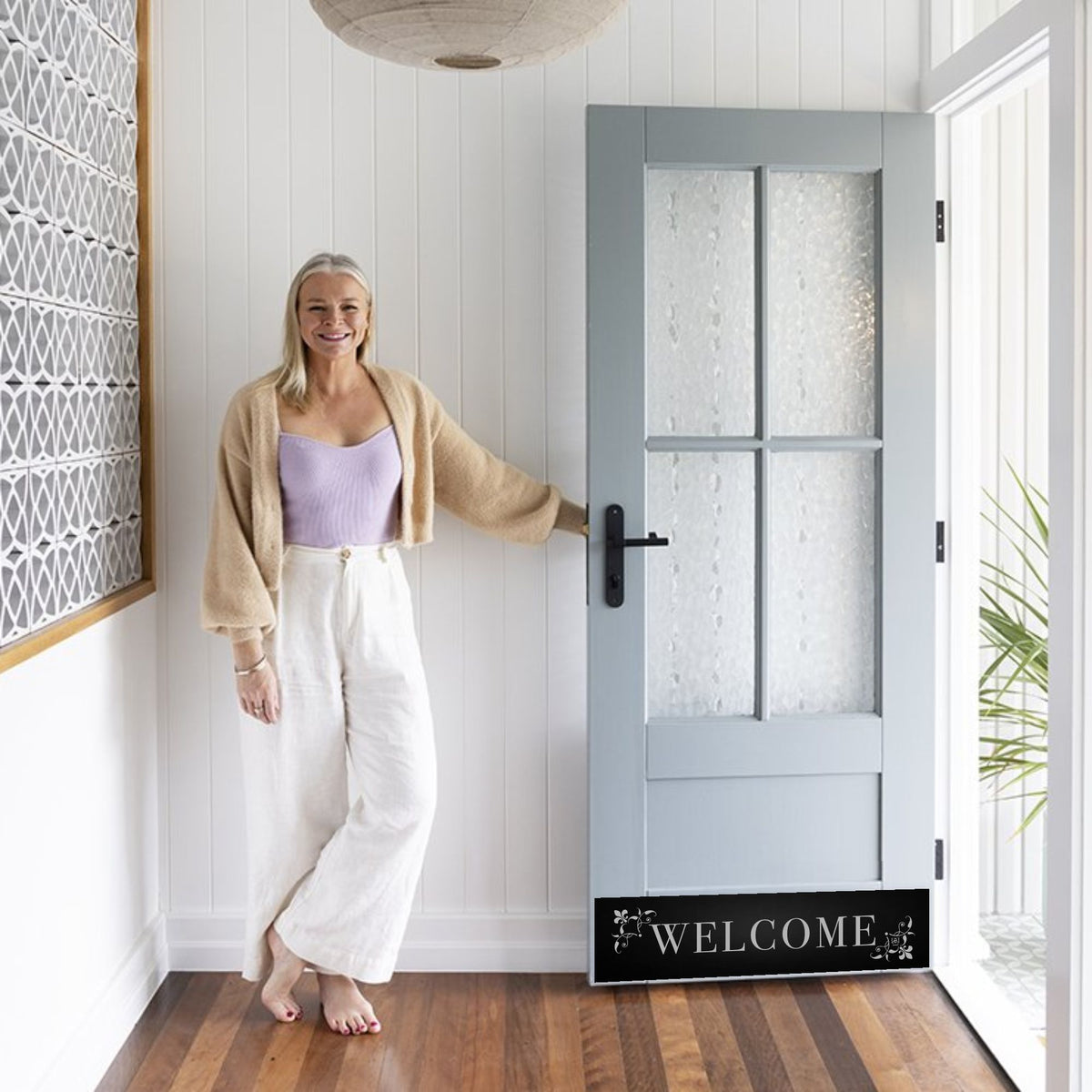 Woman holding open home door with Welcome Engraved Door Kick Plate in Satin Black 
