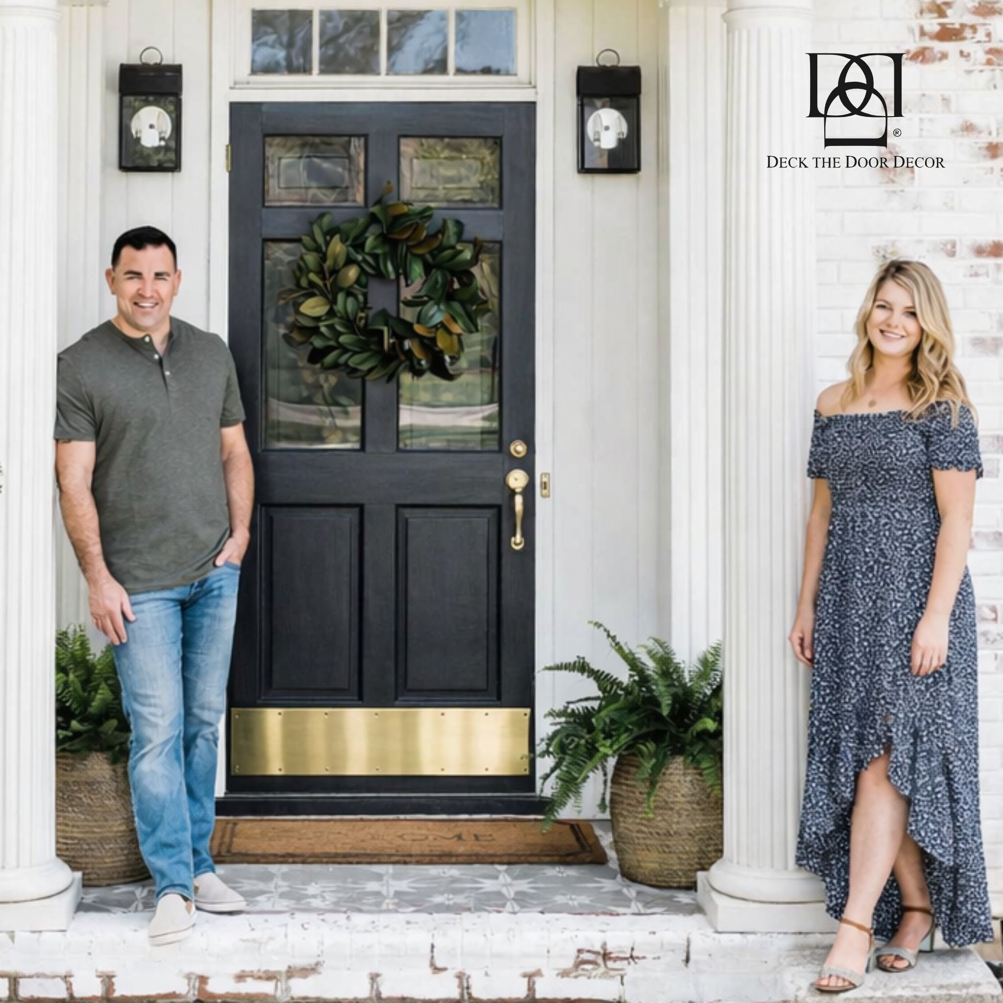 A man and a woman stand on the front steps beside a black front door with a  brass door kick plate.