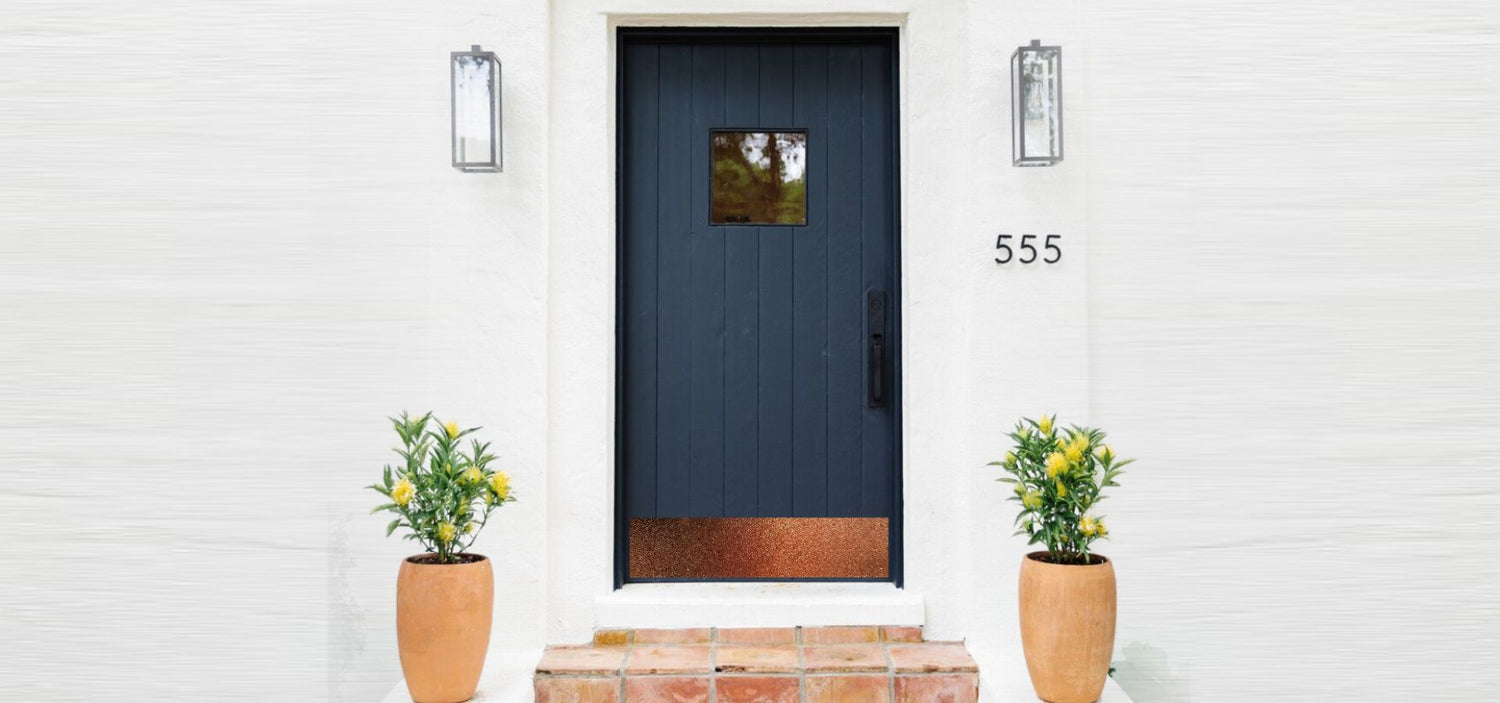 A modern navy blue front door with a hammered copper kick plate